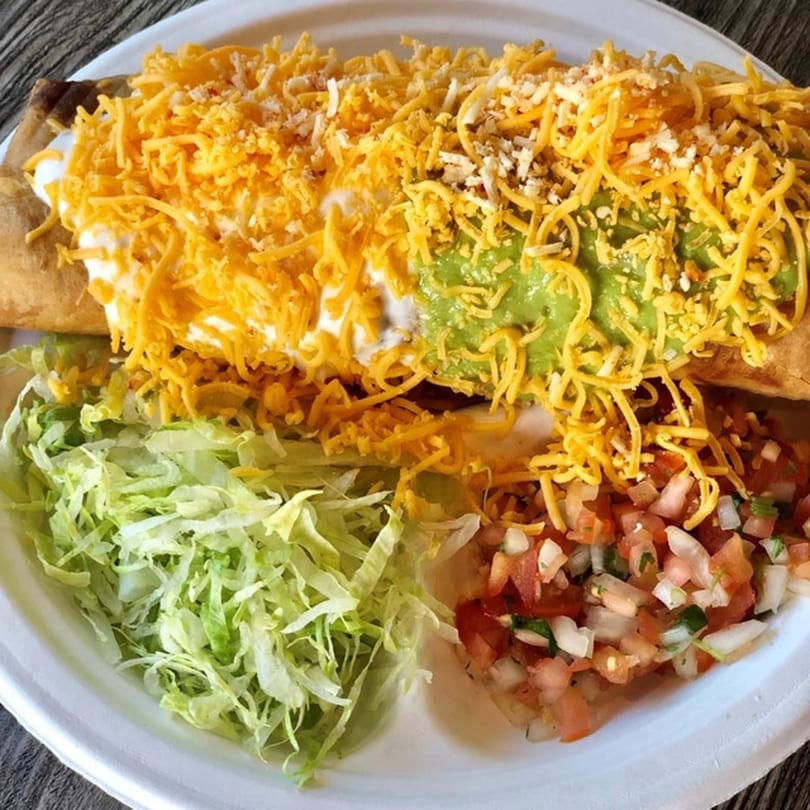 A large Roberto's Taco Shop burrito covered in cheese, sour cream, and guacamole, with sides of lettuce and pico de gallo.