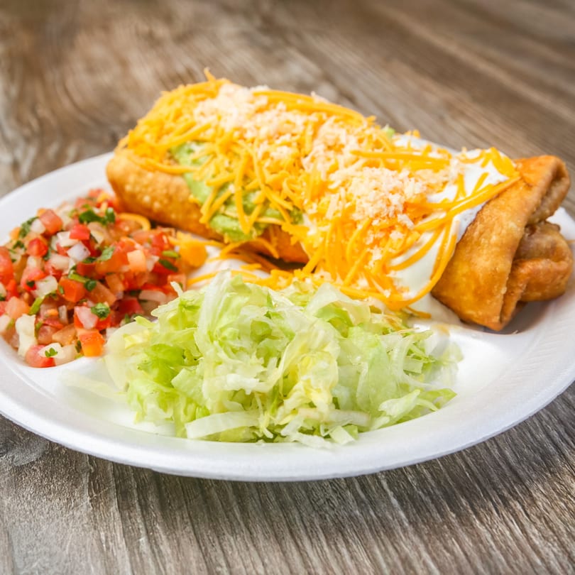 A deep-fried burrito topped with cheese, sour cream, and guacamole, served with pico de gallo and lettuce.