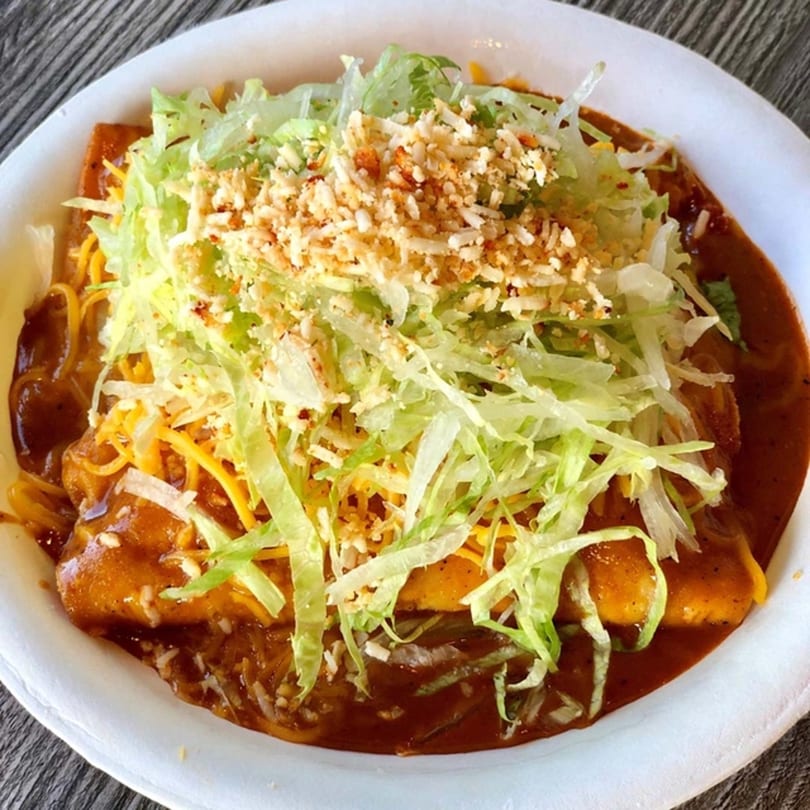 Roberto's Taco Shop enchiladas covered in red sauce, shredded lettuce, and cheese in a white bowl.